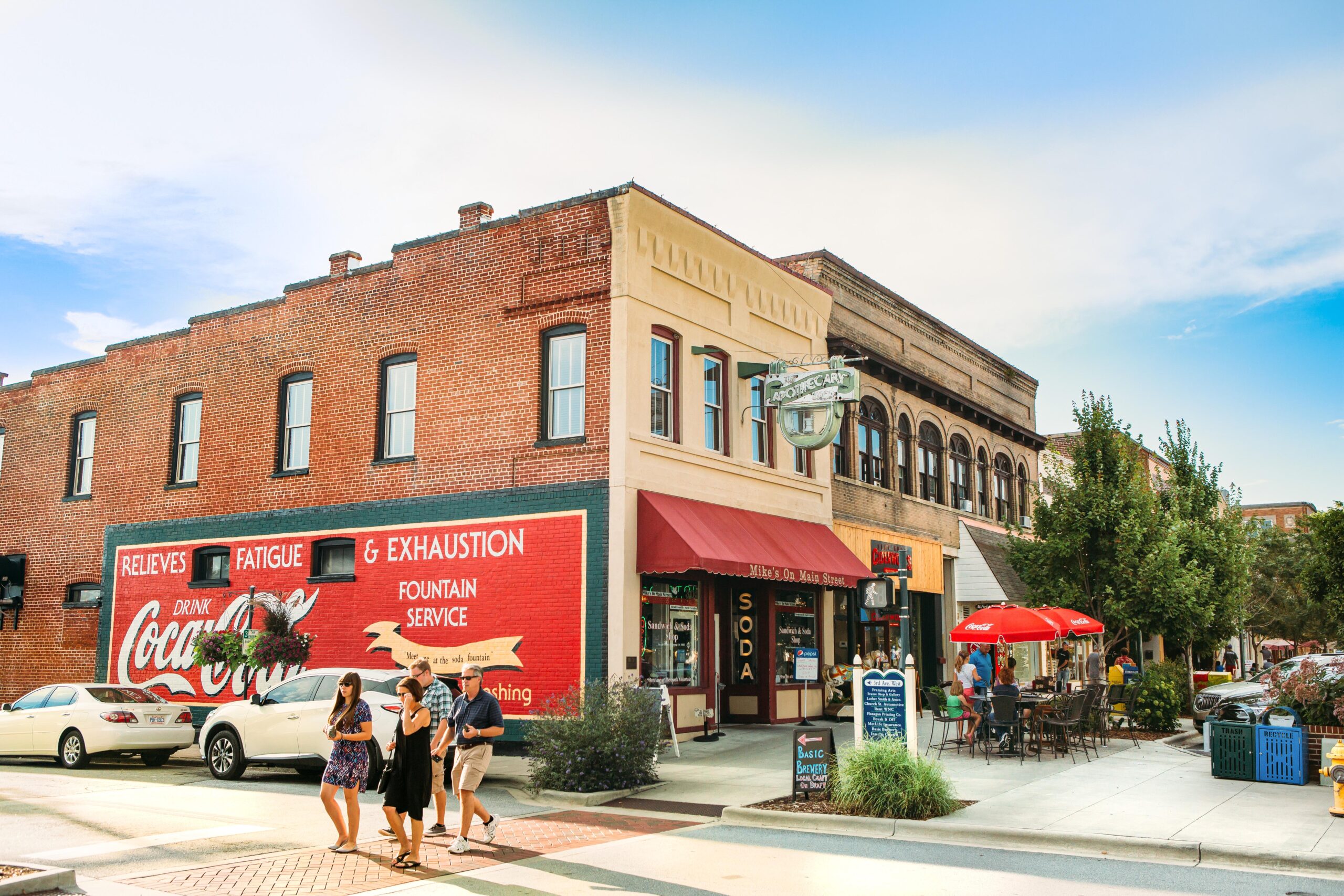 people crossing the street in front of a big coc-a-cola mural painted on a brick building